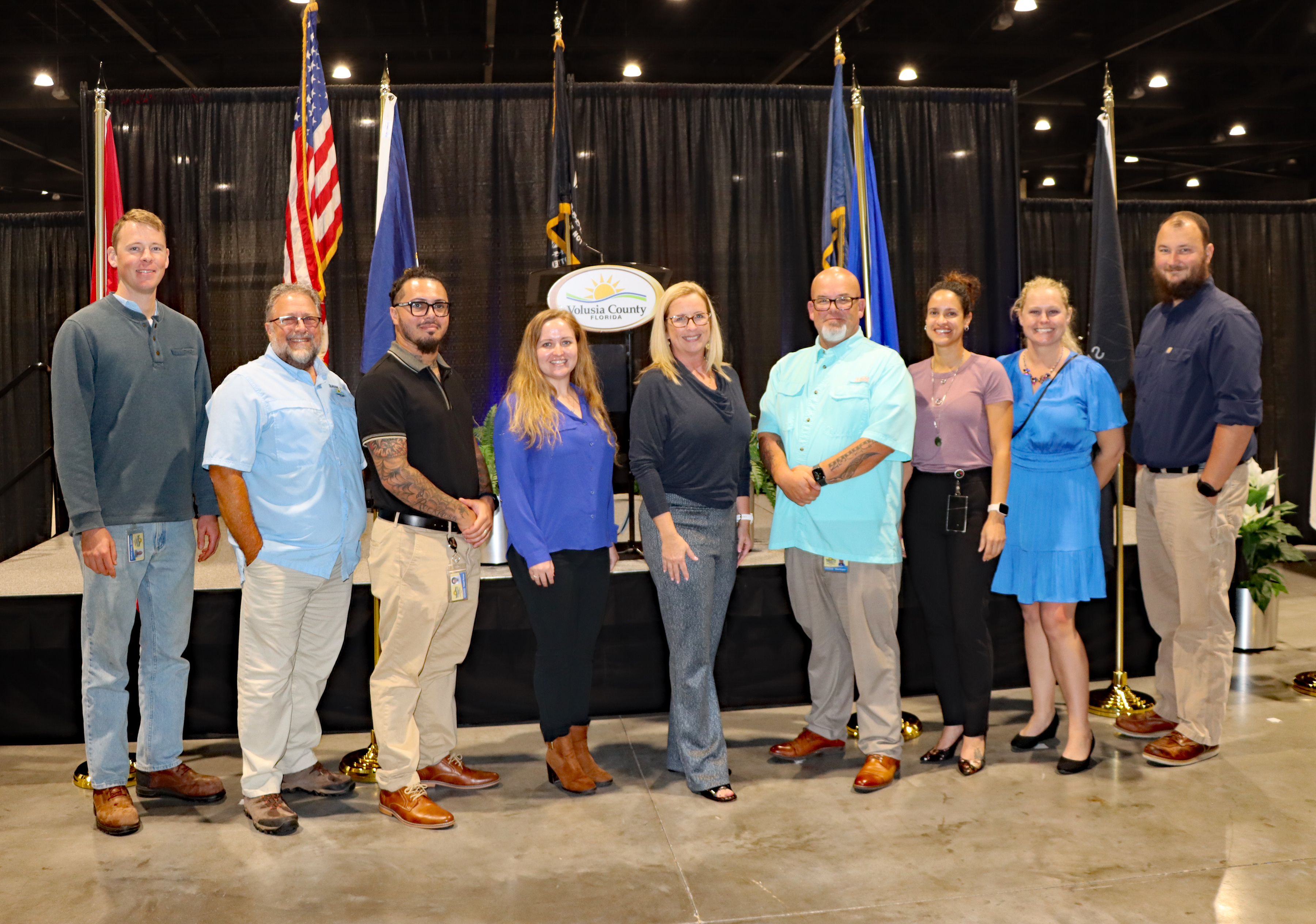 Transform386 Veteran Staff Members stand in a line behind an American flag smiling.